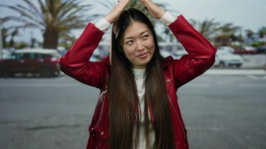 Kırmızı ceketli kadın arka planda bulanık arabalarla şehir caddesinde neşe içinde poz veriyor..