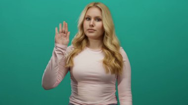 Yeşil arka plana karşı yemin etmek için elini kaldıran kadın pembe gömlek giyiyor profesyonel ortamda özgüven ve samimiyeti yansıtıyor odaklanmış ifade ile..