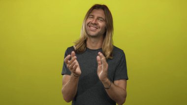 Sarı renkli bir stüdyoda gülümseyen ve alkışlayan sarışın adam, kutlama onayını destekliyor..
