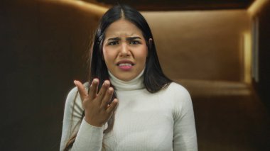 Salon ortamında belirsizlik ve tefekkürün göstergesi olarak tarafsız bir arka planda kafa karışıklığını ifade eden genç bir kadın..