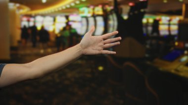 İçeriden aydınlatılmış kumar makineleriyle dolu canlı bir kumarhaneye uzanan bir adamın eli potansiyel başarı ve heyecan öneriyor..