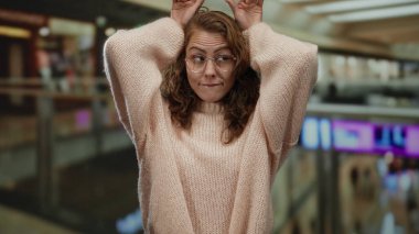 Kapalı bir alışveriş merkezinde, elleri gözlüklü, süveteri kapalı bir alışveriş merkezi atmosferi ve bulanık dükkanlarla çevrili bir şekilde sürpriz yapan bir kadın..