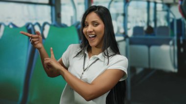 Otobüsün içinde hareketler yapıp gülümseyen genç bir kadın yeşil ve mavi koltuklu rahat bir ortamda canlı bir hareket ve ifade sergiliyor..