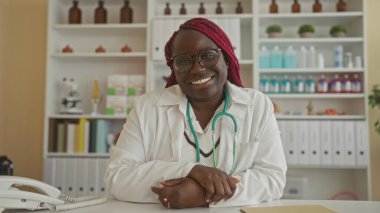 Steteskop ve arkaplanda dosyalarla klinikte gülümseyen kadın doktor, konsültasyonlar ve sağlık hizmetleri için uygun bir karşılama ortamı öneriyor..