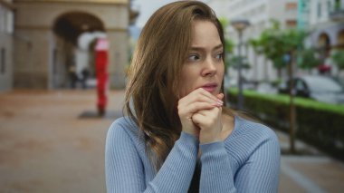 Bulanık arabaların ve sokak lambalarının arasında ellerini sıkan gergin ifadeye sahip genç beyaz kadın; endişe.