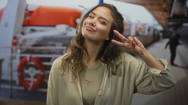 İspanyol kadın bir yolcu gemisinin güvertesinde canlı hayat halkaları ve okyanus zeminiyle barış işareti yapıyor. Genç enerjisiyle deniz kenarında neşeli bir anı yakalıyor..