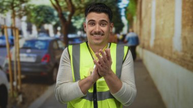 Şehir caddesinde yansıtıcı yelek giymiş İspanyol bir adam. Bulanık arabalar ve ağaçlarla dolu bir şehir ortamında gönüllü ruhu somutlaştırıyor..