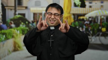 Papaz kıyafeti giyen Asyalı bir adam açık hava kafesinde canlı şehir geçmişiyle gülümsüyor ve neşeli bir dini tema öneriyor..