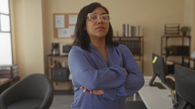 Bir ofis binasında kolları çapraz duran gözlüklü bir kadın..