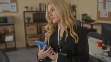 Ofis ortamında tablet kullanan sarı saçlı bir kadın, raflar, kitaplar ve bitkilerle çevrili, profesyonel ve odaklanmış bir çalışma ortamı sağlıyor..