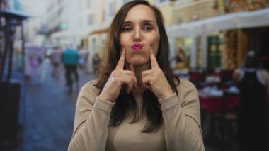 Genç İspanyol kadın açık hava restoranında parmaklarıyla yanaklarına dokunuyor; neşe dolu..
