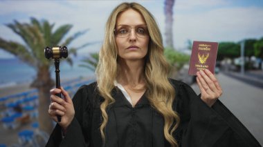 Genç sarışın kadın yargıç elinde Tayland ve pasaport ve tokmak ile deniz kenarında bir sahilde, yasal temalı uluslararası bir açık hava ortamında kanun ve düzeni tasvir ediyor..