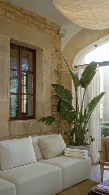 İçinde yastıklar, büyük saksı bitkileri, taş duvarlar, kemerli pencereler ve zarif dekorlar bulunan rahat, şık bir atmosfer yaratan Akdeniz ev içi koltuklar..