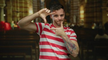 Kilisedeki genç adam çerçeveli elleriyle gülümsüyor. Kilisenin iç tarafında çizgili tişört giyiyor. Gün içinde evde yaratıcılık ve pozitiflik olduğunu gösteriyor..