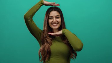 İspanyol kadın gülümsüyor ve elleri başının üstünde, canlı yeşil bir arka plan duvarına karşı izole bir şekilde bir çerçeve hareketi yapıyor..