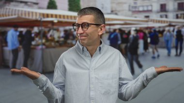 Dışarıdaki hareketli sokak pazarında canlı pazar ortamında günlük gömlek ve gözlük takan insanlarla çevrili bir adam.