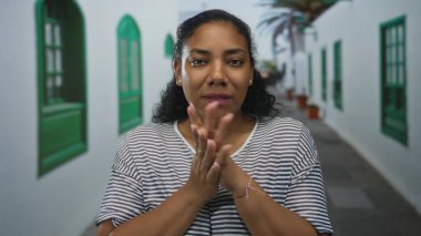 Beyaz duvarlar ve yeşil pencere panjurları ile çevrili dar eski kasaba caddesinde dururken avuçlarını ovuşturan Afrikalı Amerikalı kadın..