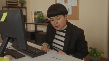 Ofiste çizgili bir kazak ve spor ceket giyen, bilgisayar ve masa odaklı, kitaplarla ve raflardaki bitkilerle çevrili, verimli bir atmosfer yaratan bir kadın..