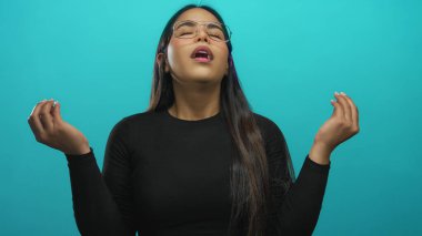 Kadın sakin bir şekilde meditasyon yapıyor gözleri kapalı ve elleri mudra pozisyonunda izole edilmiş yeşil bir arka plan üzerinde, sakin bir ortamda gözlük ve siyah kıyafetler giyiyor..