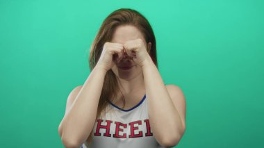 Kırmızı harflerle beyaz üniforma giyen amigo kadın yeşil stüdyoda yorgun gözleri yumruklarla siliyor..