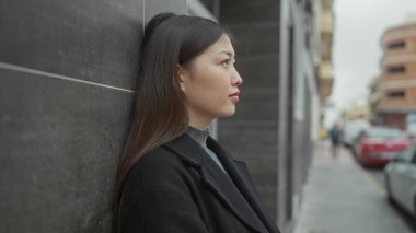 Şehir caddesinde duran kadın duvarlara yaslanıyor şehir arka planında bulanık bir görüntü yansıtıyor..