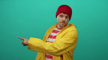 Sarı yağmurluk giyen İspanyol genç adam yeşil arka plana karşı küçümseyici bir jest yapıyor..