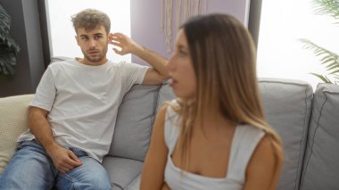 Parlak bir oturma odasındaki kanepede oturan erkek ve kadın, evdeki rahat atmosferi geliştiren bitkiler ve ince dekorasyonlarla sakin ve samimi bir anı öneriyorlar..