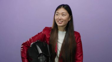 Stüdyoda kaskını tutarak gülümseyen bir kadın zarif kırmızı ceketiyle modern yaşam tarzını aktaran münferit mor arka plana karşı..