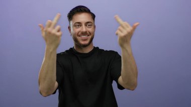 Sakallı genç adam gülümserken orta parmaklarıyla jestler yapıyor, izole edilmiş mor arka plana karşı duruyor..