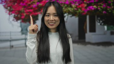 Dışarıdaki genç kadın renkli çiçeklerle çevrili canlı bir sokakta coşkuyla havayı yakalıyor..