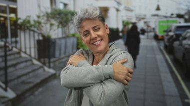 Gri kapüşonlu ve nazikçe gülümseyen kollarını göğsüne dolamış bir kadın..