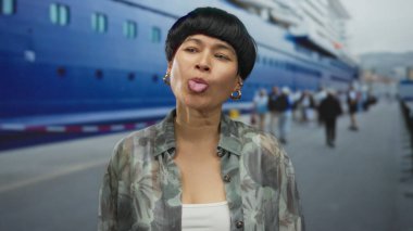 Sahilde gülümseyen ve dil uzatan Çinli bir kadın. Arka planda gezinti, neşeli duygular sergiliyor..