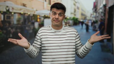 Şehrin hareketli bir caddesindeki terasta duran adam rahat bir restoranın önünde açık şehir ortamında rahat ve kendinden emin bir hava yayıyor..