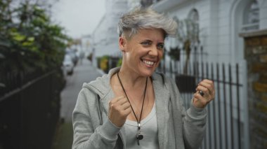 Açık gri kapüşonlu kadın sokakta dijital gümüş kronometreyi kontrol ediyor..