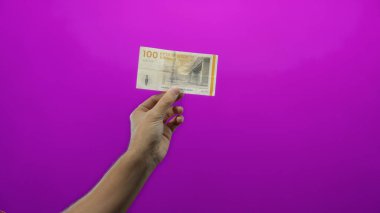 Danimarka Kronu 'nu elinde tutan adam, izole edilmiş, mor arka planda, modern tasarım unsurları olan bir para birimi gösteriyor..