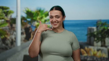 Bana işaret eden bir kadın, yeşil gömlekli, gülümseyen, açık hava, tropikal ortam, gündüz kuşağı, neşeli, rahat atmosfer..