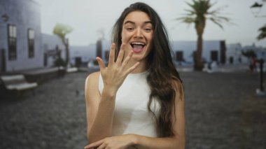 Gülümseyen genç İspanyol kadın, parlak bir sabahta palmiye ağaçlarının altında sokakta beş parmak sayıyor..