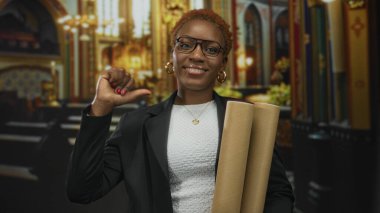 Blazer ceketli kadın elinde mimari planlar ile kilisenin iç dekorasyonunun içini başparmağıyla göğsüne işaret ediyor..