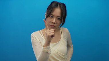 Genç Çinli kadın kendinden emin ifadeyi tasvir eden izole edilmiş mavi arka plan duvarını işaret ediyor..