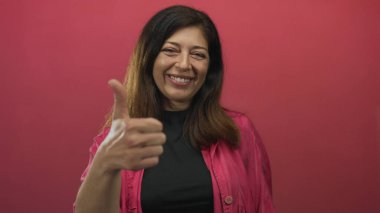 Pembe ceket giyen ve gülümseyen İspanyol bir kadın pembe bir geçmişi olan bir stüdyoda onay veriyor..