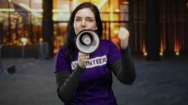 Açık havada esmer bir kadın sokakta megafon diye bağırıyor. Mor gönüllü tişörtü giyiyor. Coşku ve amaç taşıyor..