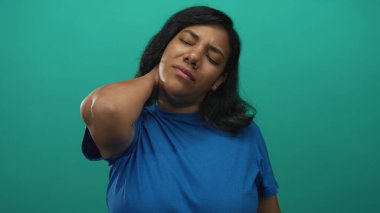 Bir eliyle boynu tutan, gözleri kapalı ürkek, mavi gömlek giyen bir kadın var..