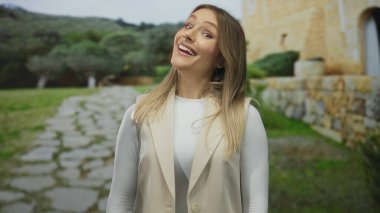 Parkta taş yolu ve yeşilliği olan bir kadın, kırsal manzaranın ortasında tarafsız ifadeler sergiliyor, basitliği ve doğal çevreyi vurguluyor..