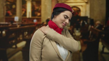 Üniformalı İspanyol kadın uçuş görevlisi kilisenin içinde ayakta duruyor omuzlarını kavrıyor yorgun ve dingin bir görünüm takınıyor geleneksel dini zemini harmanlıyor..