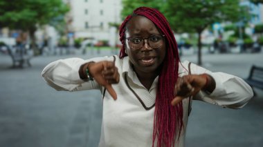 Arka planda ağaçlar ve binalar olan bir şehir caddesinde şehir yaşamını ve duygularını sergileyen bir kadın tasvip etmiyor..