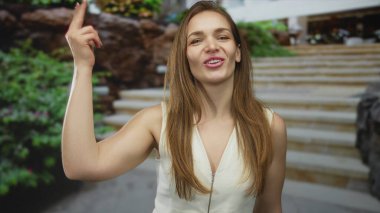 Genç beyaz kadın elini dudaklarına bastırıyor ve bir sokakta parlak güneş ışığı altında bir öpücük veriyor..