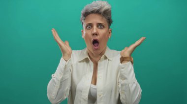 Beyaz gömlekli kadın, turkuaz stüdyoda ağzı açık el kaldırıyor. Sürpriz..