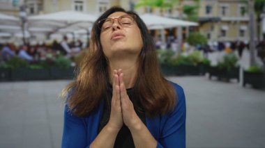 Avuç içli bir kadın, şehir binasının önündeki bir restoranın terasında dua jestinde birbirine bastırılmış..