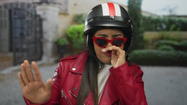 Motosikletli genç Latin bir süvari kötü kokuya tepki verirken, kadın dışarıda yüzünü kapatırken burnunu sıkıyor..