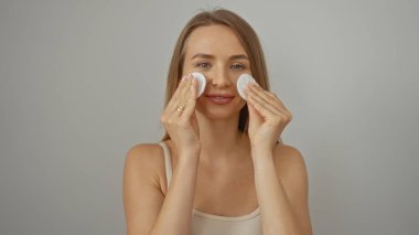 Beyaz arka planda izole edilmiş pamuk pedlerle yüzünü temizleyen kadın cilt bakımını ve kadınlığı vurguluyor.